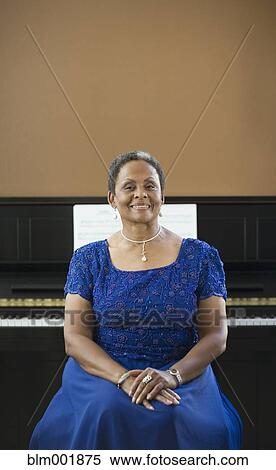 Stock Photography - African woman in evening gown sitting in front of piano. Fotosearch