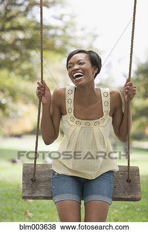 Stock Photo - African woman laughing on swing in park. Fotosearch
