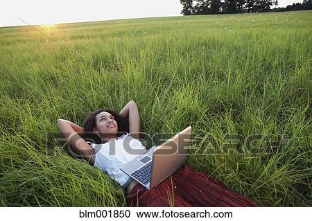 Stock Image - African woman laying in meadow with laptop. Fotosearch