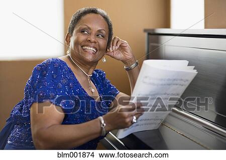 Picture - African woman leaning on closed piano. Fotosearch