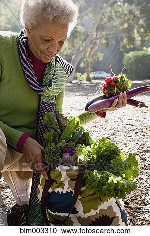 Stock Image - African woman putting vegetables into bag. Fotosearch