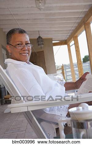 Stock Photograph - African woman reading a book on porch. Fotosearch