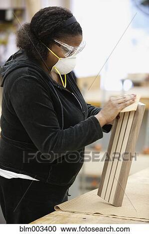 Stock Image - African woman sanding wood in workshop. Fotosearch