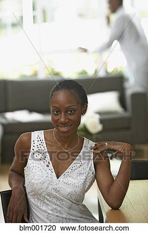 Stock Image - African woman sitting with husband in background. Fotosearch