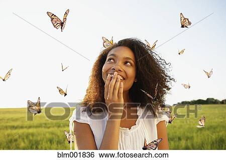 Stock Photograph - African woman standing among butterflies in meadow. Fotosearch
