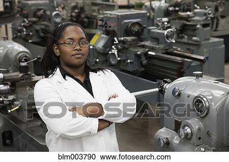 Stock Image - African woman standing in machine tooling plant. Fotosearch
