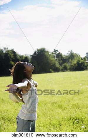 Stock Image - African woman standing in meadow with arms outstretched. Fotosearch