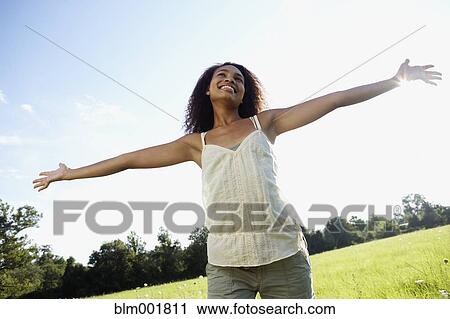 Stock Image - African woman standing in meadow with arms outstretched. Fotosearch