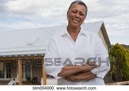 Stock Image - African woman standing outside house. Fotosearch