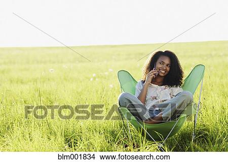 Picture - African woman using cell phone in meadow. Fotosearch