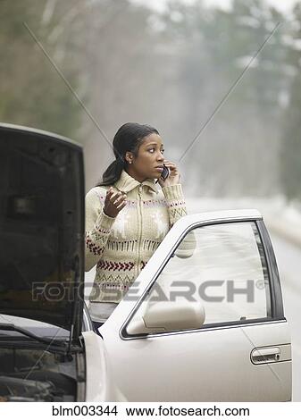 African woman using cell phone next to car with hood up View Large Photo Image Picture - African woman using cell phone next to car with hood up. Fotosearch