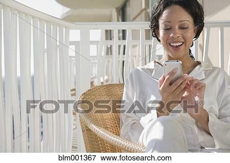 Stock Photo - African woman using cell phone on balcony. Fotosearch