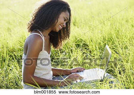 Stock Photography - African woman using laptop in meadow. Fotosearch