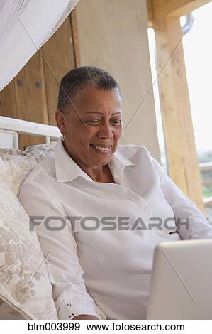 Stock Photo - African woman using laptop on bed. Fotosearch