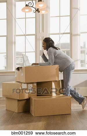 Stock Photo - African woman using laptop on boxes. Fotosearch