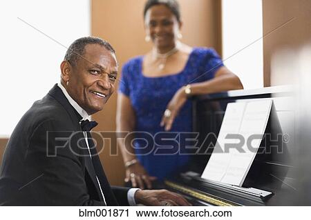 Stock Image - African woman watching african man play piano. Fotosearch
