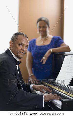 Stock Image - African woman watching african man play piano. Fotosearch