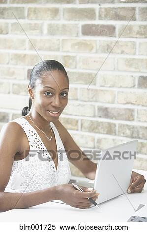 Stock Photography - African woman with laptop at table. Fotosearch