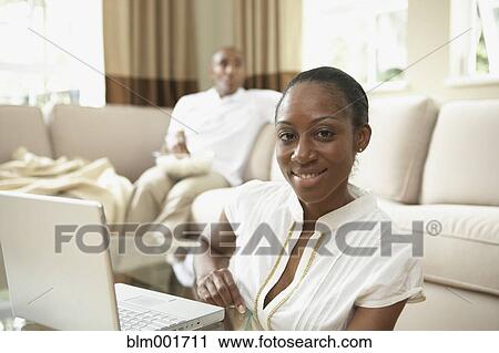 Stock Image - African woman with laptop in livingroom. Fotosearch