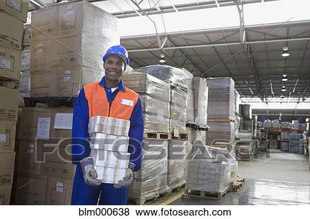 Stock Photo - African worker carrying package in warehouse. Fotosearch
