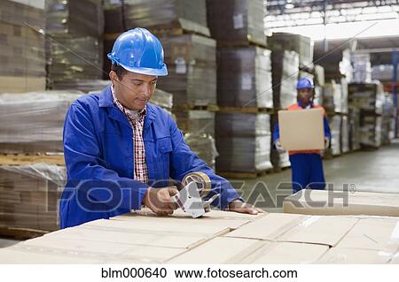 Stock Image - African worker taping boxes in warehouse. Fotosearch