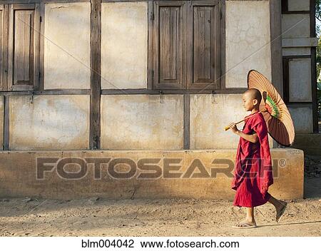Stock Image - Asian boy walking down street with sun umbrella. Fotosearch