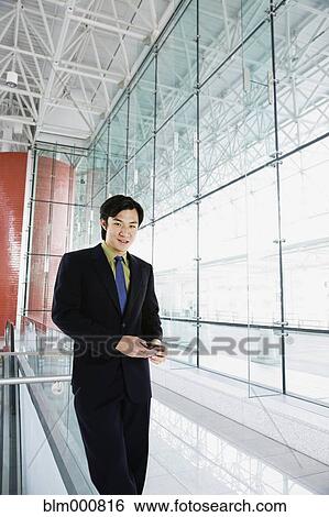 Stock Photograph - Asian businessman text messaging in airport. Fotosearch
