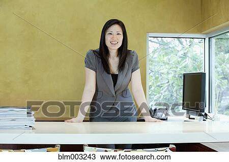 Stock Image - Asian businesswoman leaning on desk. Fotosearch