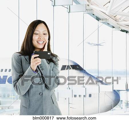 Stock Photo - Asian businesswoman text messaging in airport. Fotosearch