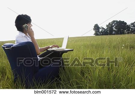 Stock Image - Asian businesswoman typing on laptop in field. Fotosearch