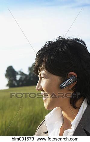 Stock Image - Asian businesswoman wearing hands-free earpiece in field. Fotosearch