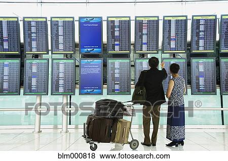 Stock Photo - Asian couple checking flight schedules in airport. Fotosearch