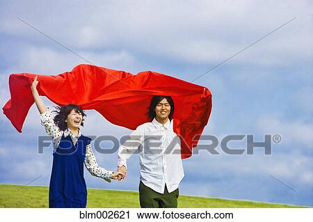Stock Image - Asian couple holding blanket in wind. Fotosearch