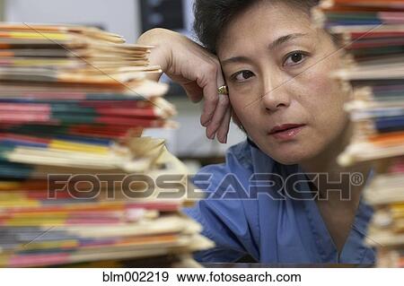 Stock Photo - Asian female medical professional looking at stack of charts. Fotosearch