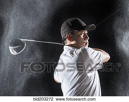 Stock Image - Asian golf player swinging club in rain. Fotosearch