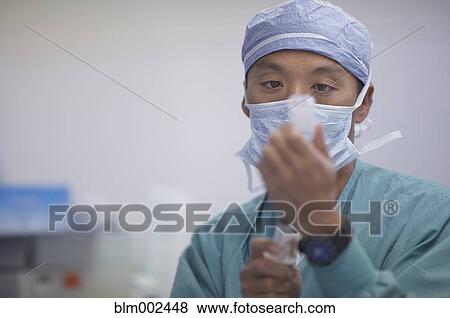 Stock Photo - Asian male medical professional filling syringe. Fotosearch