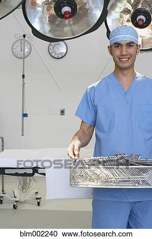 Stock Image - Asian male medical professional carrying surgical tools. Fotosearch