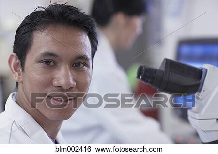 Stock Photograph - Asian male scientist next to microscope. Fotosearch