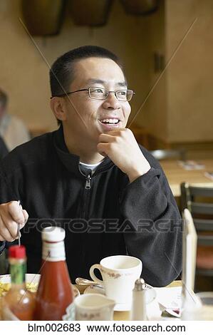 Stock Image - Asian man eating in restaurant. Fotosearch