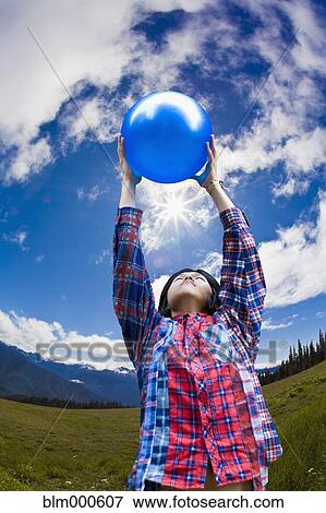 Stock Photo - Asian man lifting ball in remote field. Fotosearch