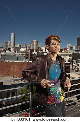 Stock Image - Asian man listening to mp3 player on urban rooftop. Fotosearch