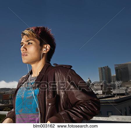 Stock Image - Asian man listening to mp3 player on urban rooftop. Fotosearch