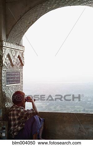 Stock Image - Asian man looking at view through binoculars. Fotosearch