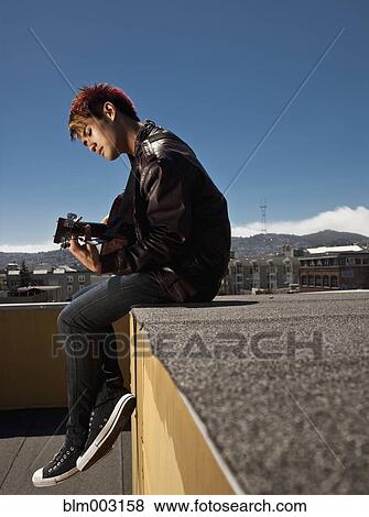 Stock Photo - Asian man playing guitar on urban rooftop. Fotosearch