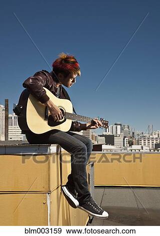 Stock Photo - Asian man playing guitar on urban rooftop. Fotosearch