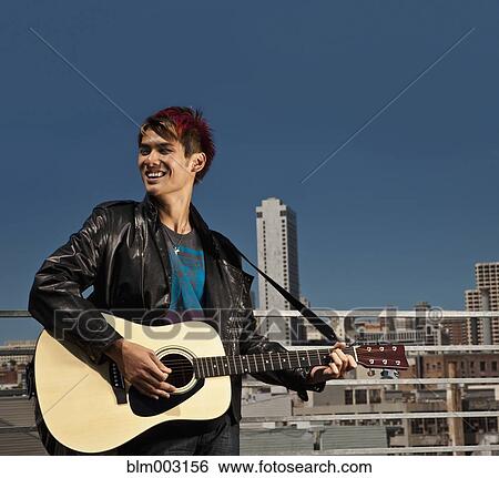 Stock Photograph - Asian man playing guitar on urban rooftop. Fotosearch