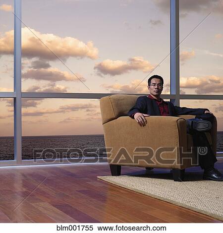Stock Photography - Asian man sitting next to window overlooking water. Fotosearch