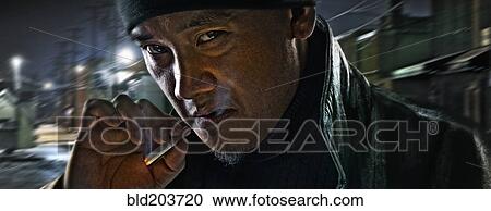 Stock Image - Asian man smoking on city street. Fotosearch