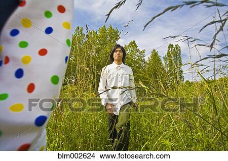 Picture - Asian man walking through tall grass. Fotosearch
