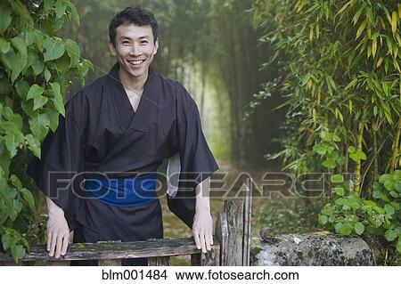 Picture - Asian man wearing traditional robe standing in forest. Fotosearch